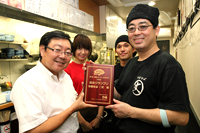 究極のラーメンAWARD選考委員長の沖山氏（写真左）から、「○丈」店主の丈六さん（右）に記念の盾が手渡された。